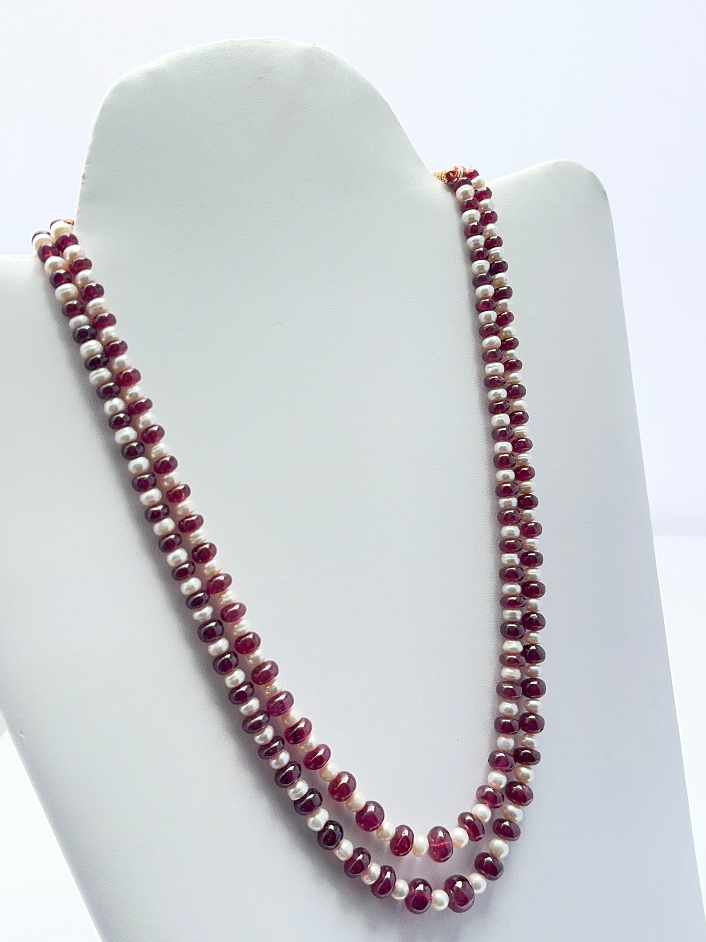 Close‑up of ruby rondelle beads and pearls arranged on a polished two‑strand necklace.
