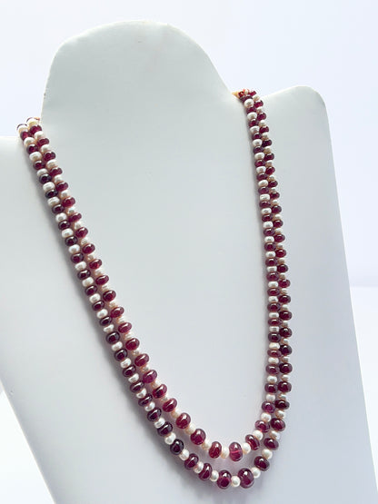 Close‑up of ruby rondelle beads and pearls arranged on a polished two‑strand necklace.