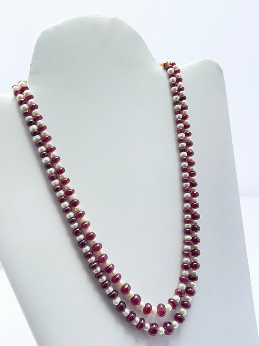 Close‑up of ruby rondelle beads and pearls arranged on a polished two‑strand necklace.