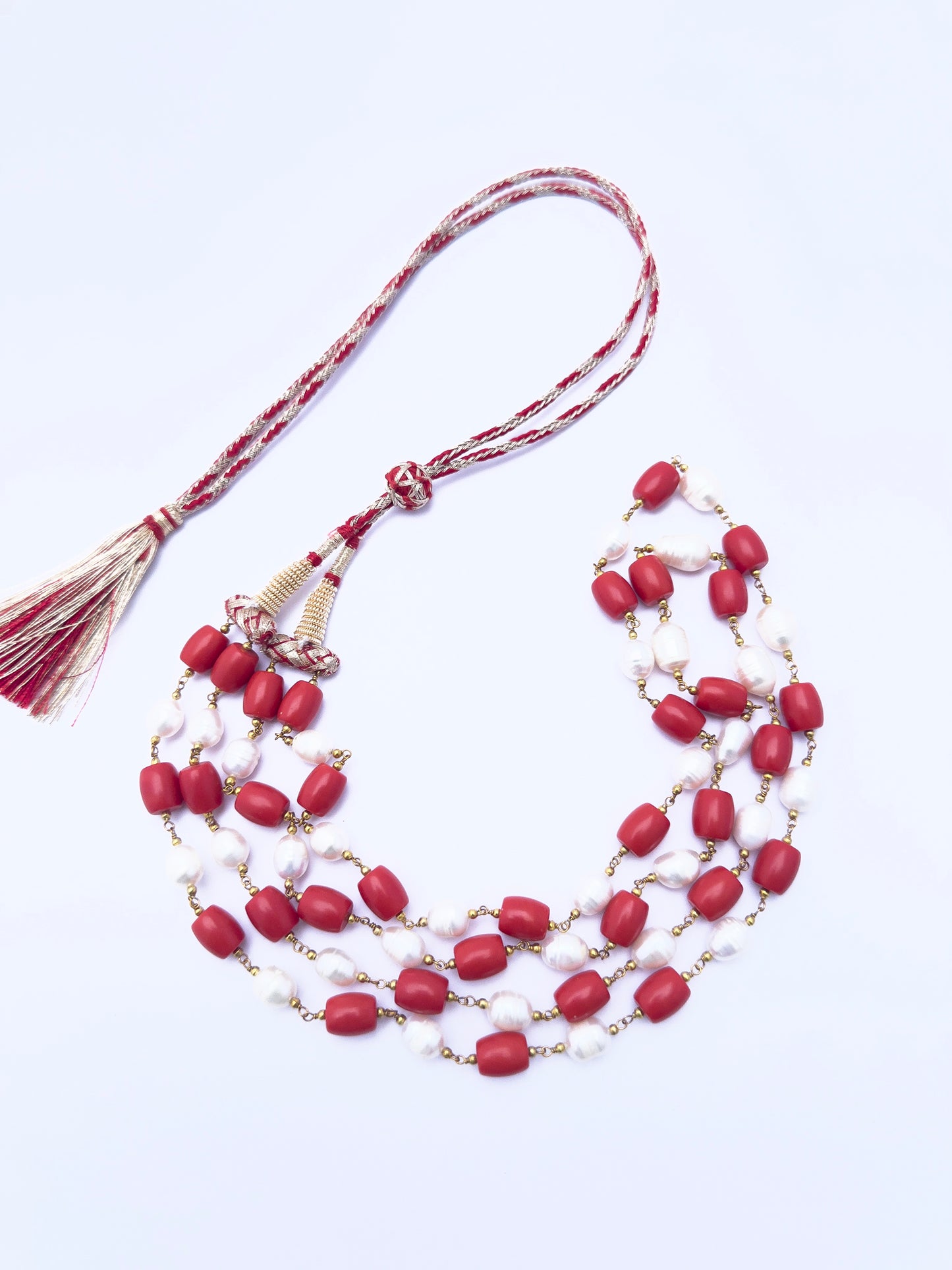 Artisan-crafted necklace featuring coral and pearls, radiant finish, adjustable silk tassel.