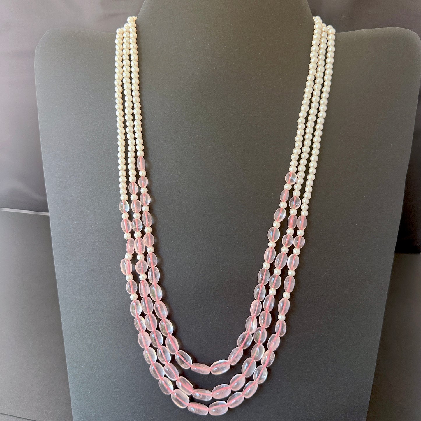 Three-strand necklace with rose quartz ovals and shell pearls in soft pink and white hues.