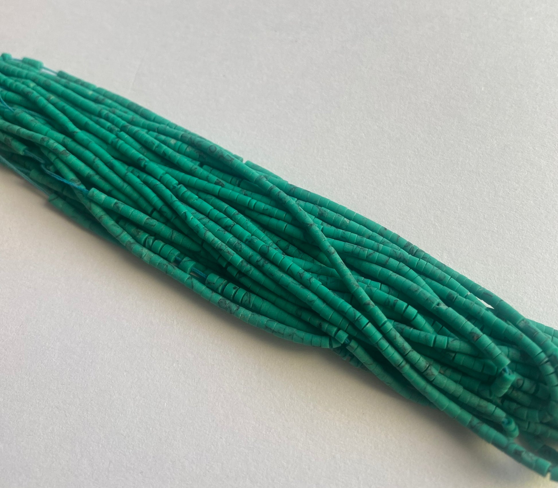 A cluster of green Afghan tube-shaped heishi beads displayed on a white surface, illustrating their distinct design and hue.