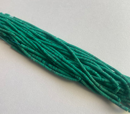 A cluster of green Afghan tube-shaped heishi beads displayed on a white surface, illustrating their distinct design and hue.