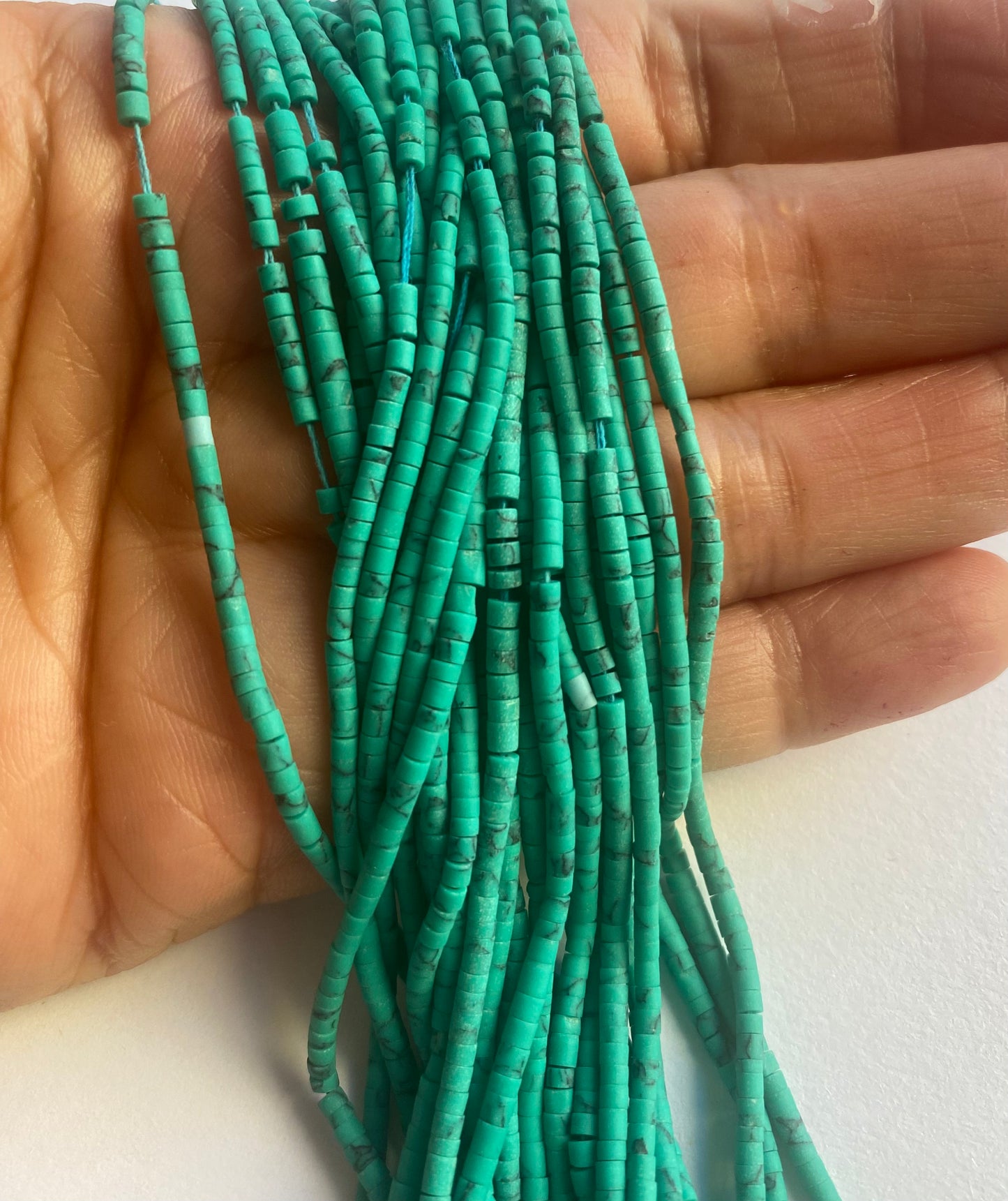 A person holding a smooth strand of Afghan Tube shaped Heishi beads, showcasing their elegant colour.
