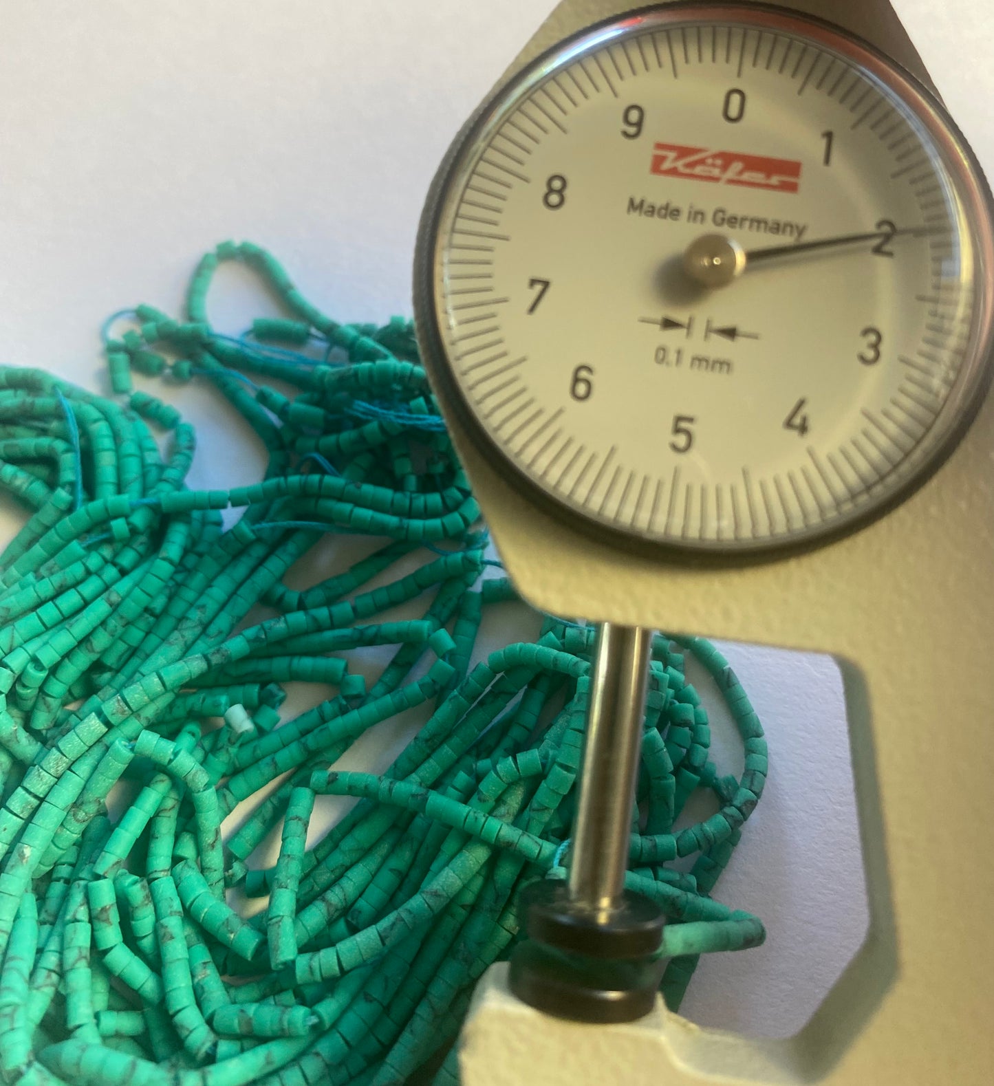 Close-up of a measuring dial gauge tool alongside a string, highlighting the precision of measurements for Afghan tube shaped heishi beads.