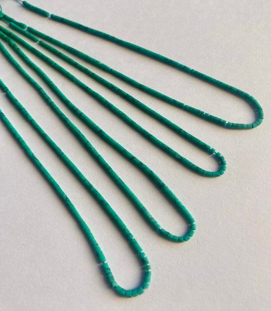 A collection of green Afghan tube-shaped heishi beads is scattered on a white background, highlighting their glossy finish