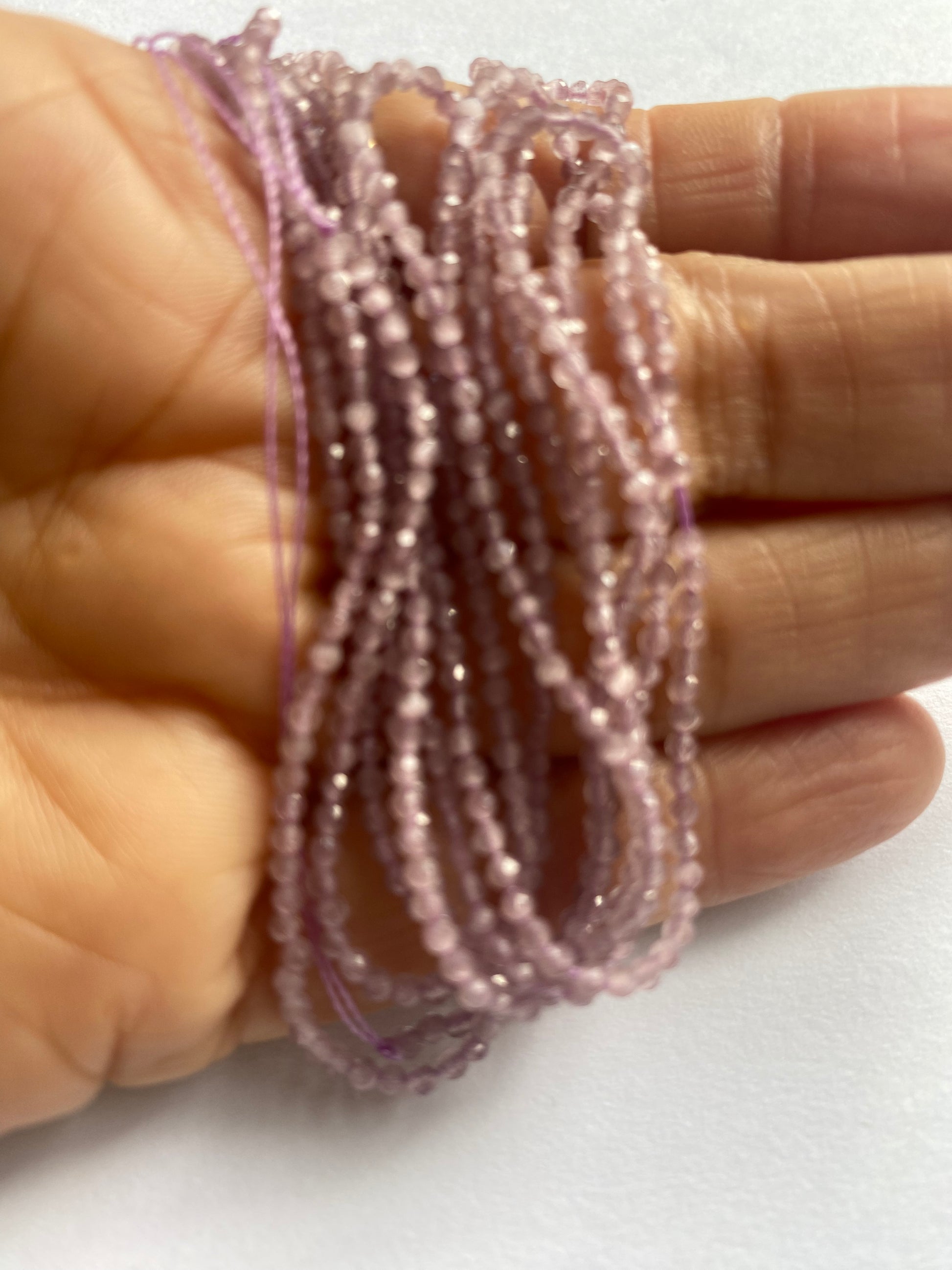 A hand displays a beautiful purple faceted rondelle amethyst gemstone beads, emphasising its faceted design and vibrant colour.