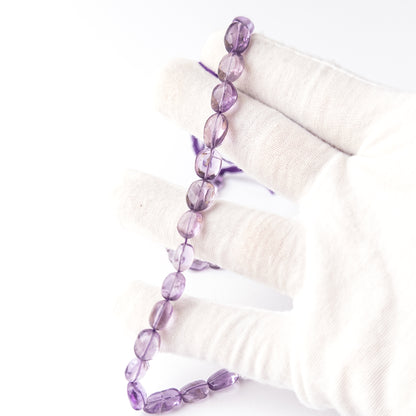 A person holds delicate strands of Amethyst beads, showcasing their smooth oval design.