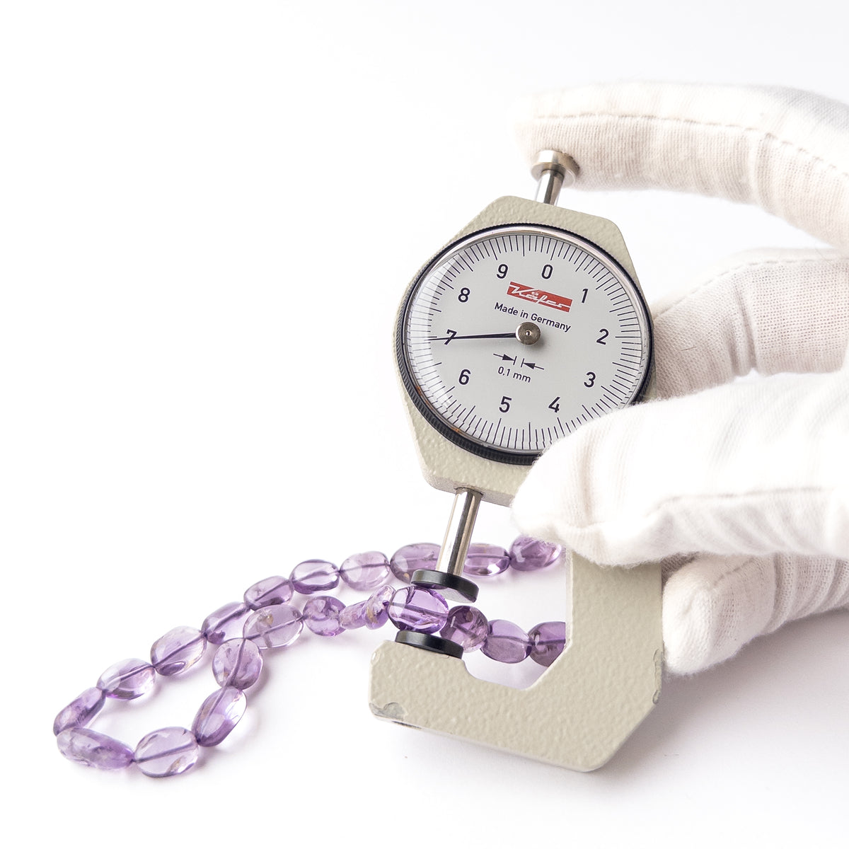 A dial gauge measures the Amethyst Smooth Oval 8.5-10mm gemstone.