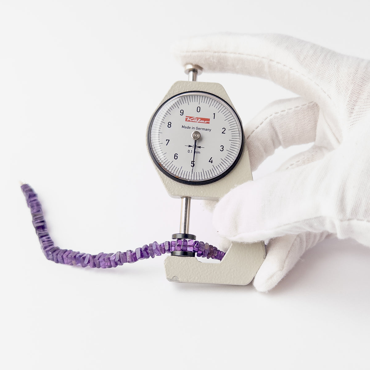 A dial gauge measures the Amethyst Smooth Square Heishi 4-5.5mm gemstone.