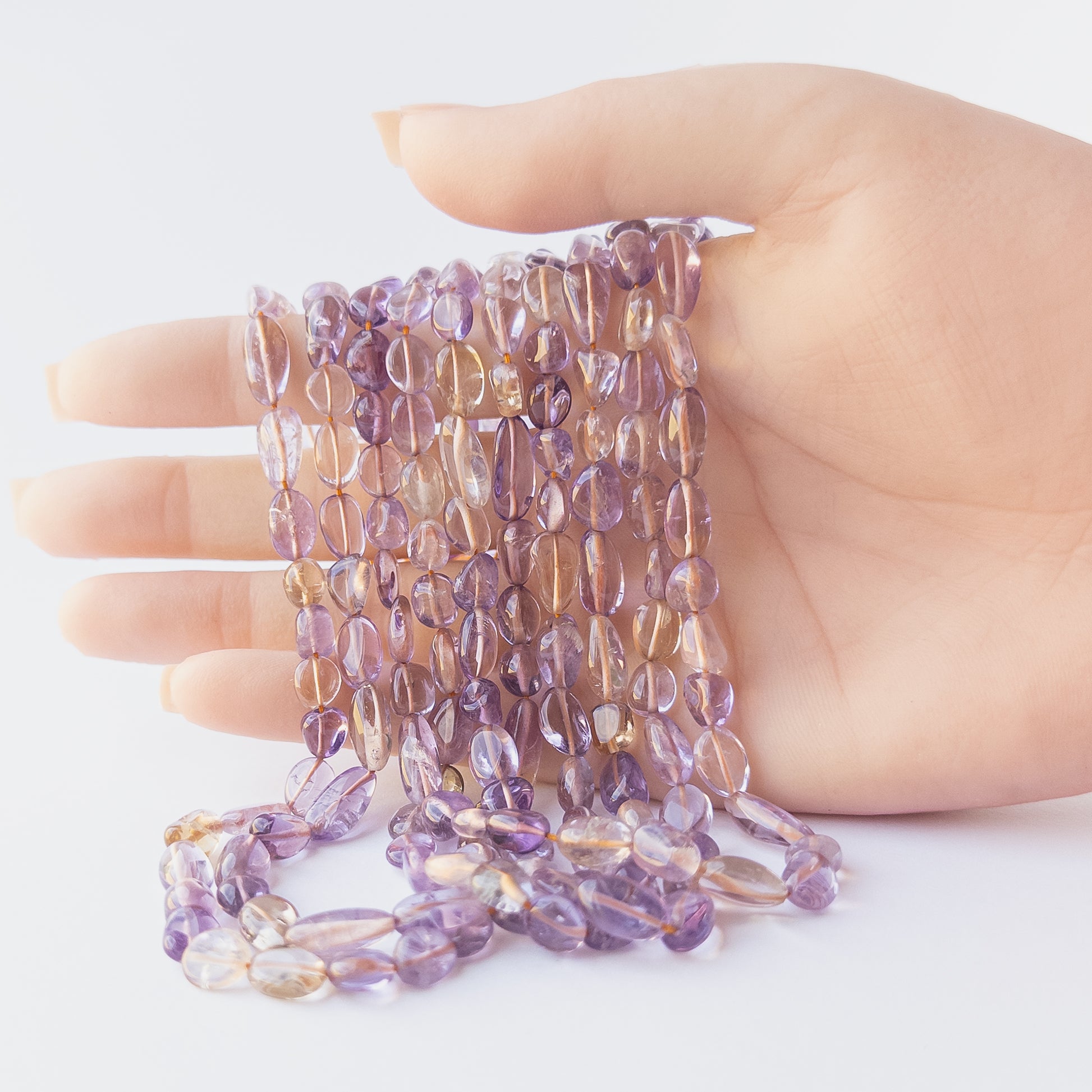 A person holds delicate strands of Ametine beads, showcasing their smooth tumble design.