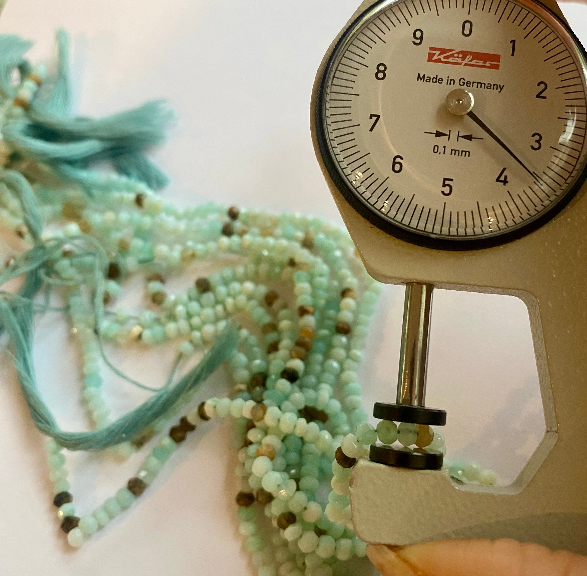 Close-up of a measuring dial gauge tool alongside a string, highlighting the precision of measurements for Aqua Sea Opal jewellery.