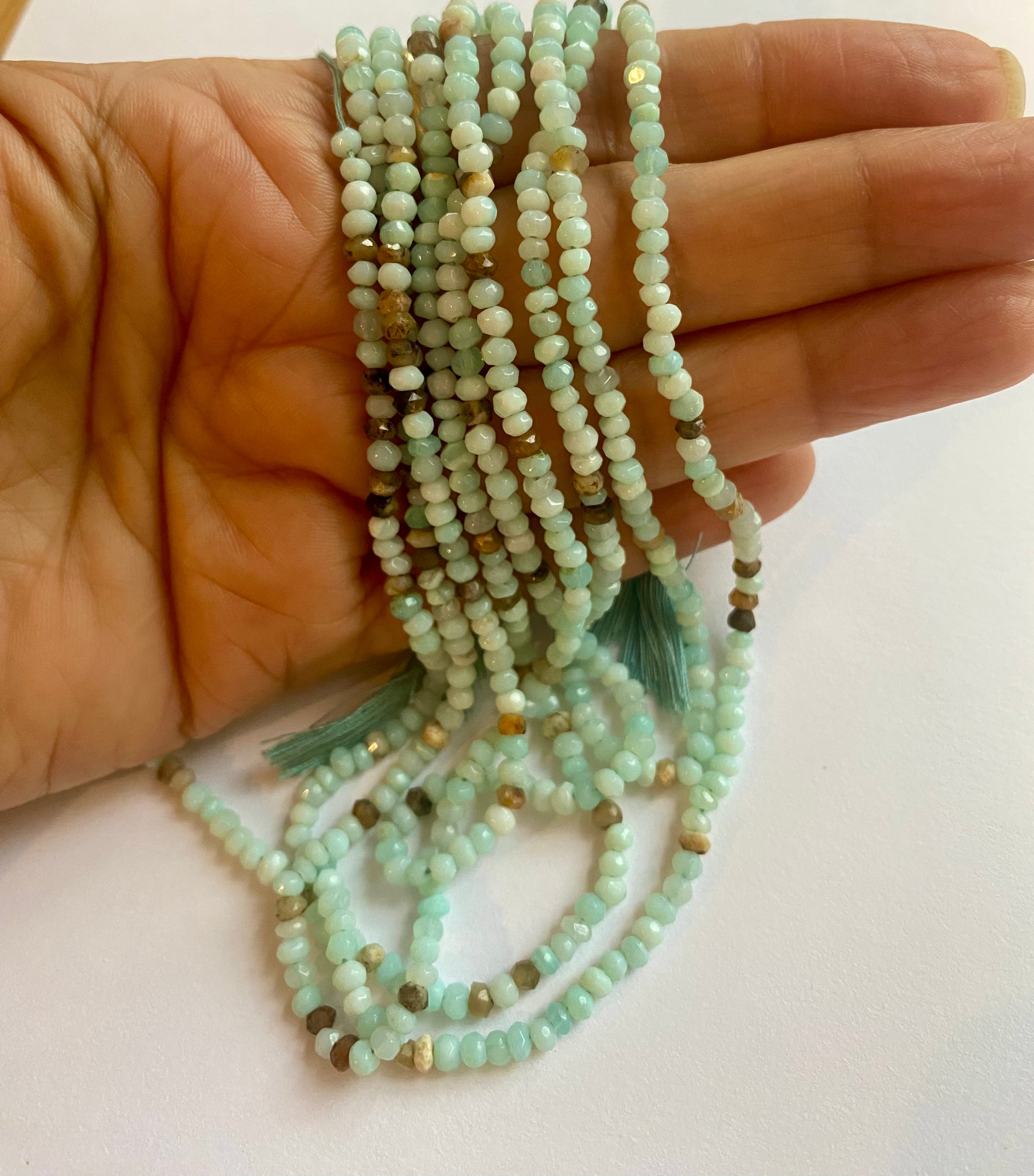 A person holding a smooth strand of Aqua Sea Opal beads, measuring 3-3.5mm, showcasing their elegant aqua colour.