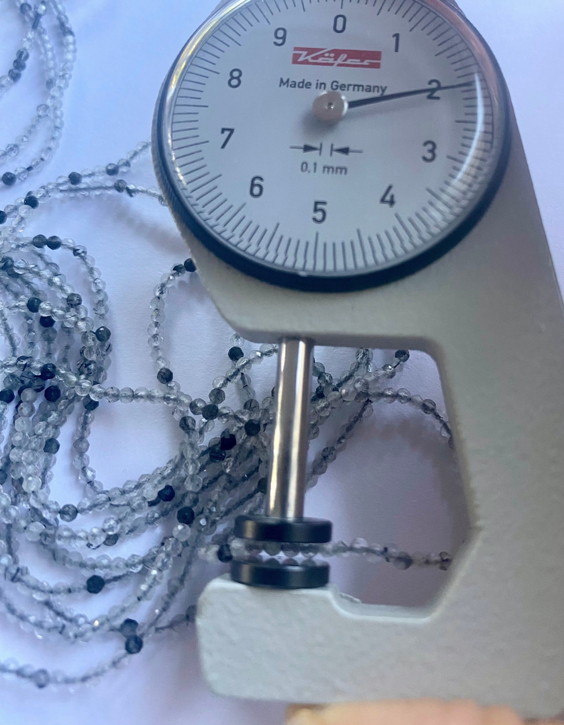 A dial gauge measures the Black Rutile Micro Faceted Rondelle 2mm gemstone.