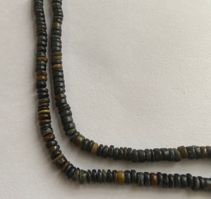  A striking strand with black tiger eye 5-5.5mm beads resting on a white surface, showcasing the vivid colours and elegant design.