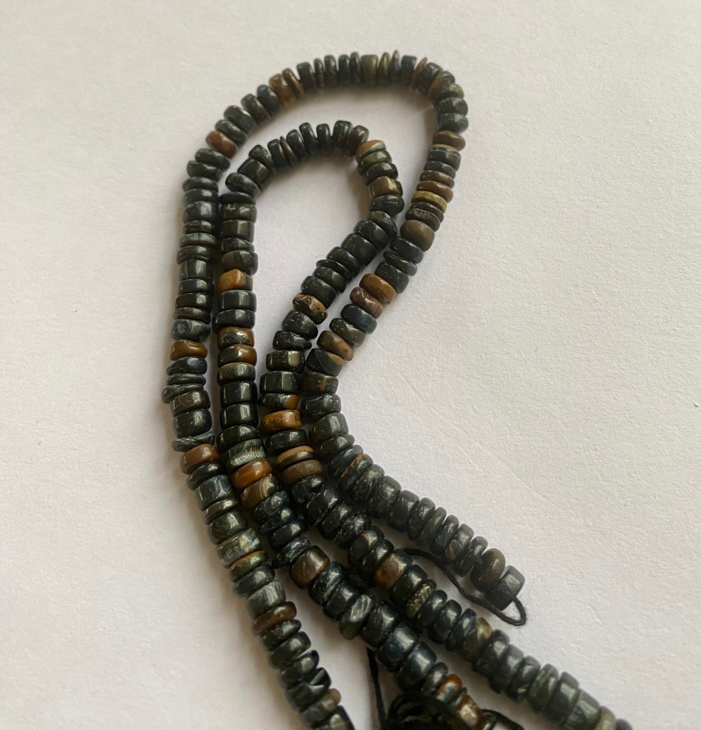  A close-up of a strand featuring black tiger eye beads displayed on a sleek white surface, highlighting its vibrant colour contrast.