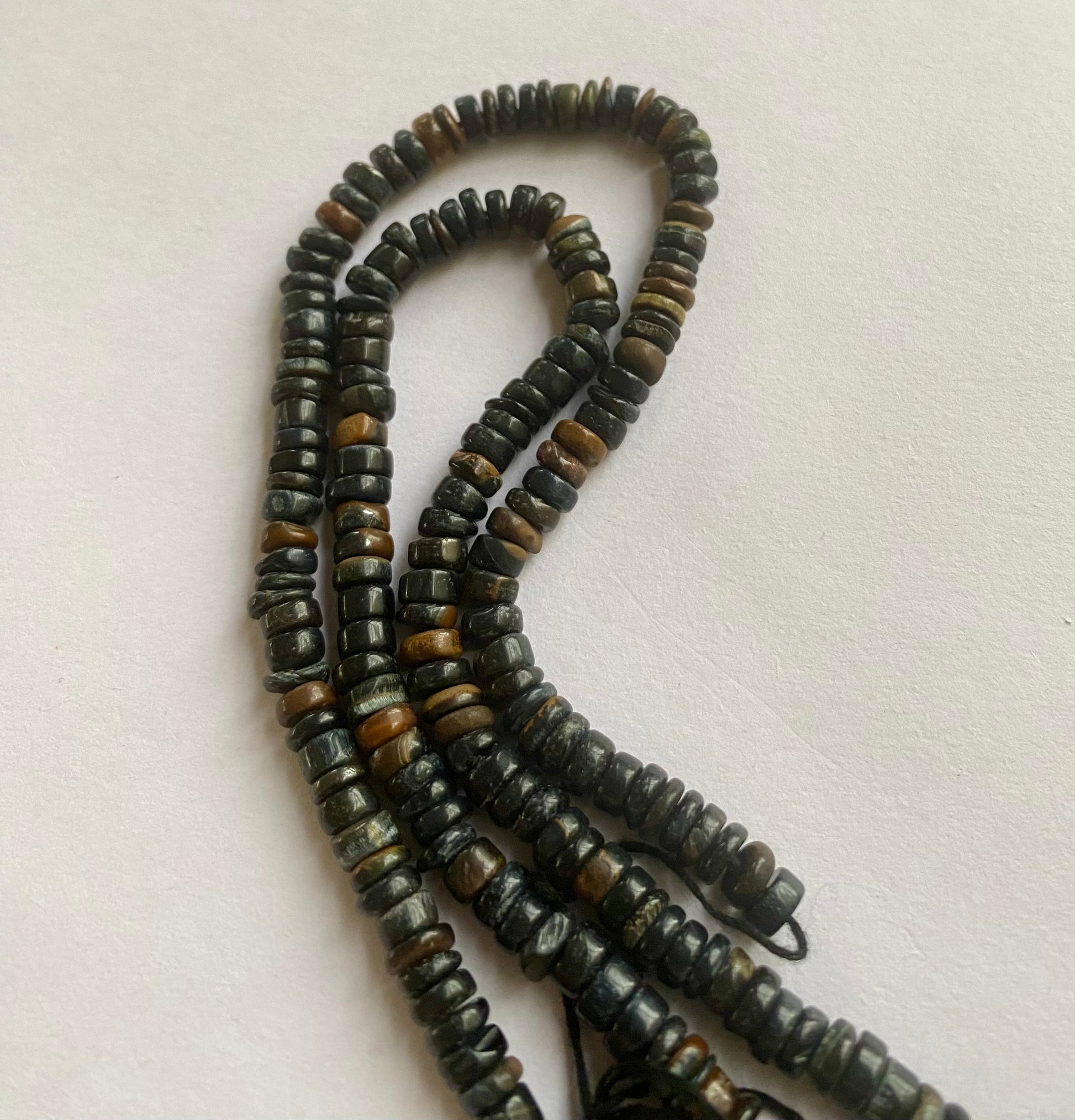  A close-up of a strand featuring black tiger eye beads displayed on a sleek white surface, highlighting its vibrant colour contrast.