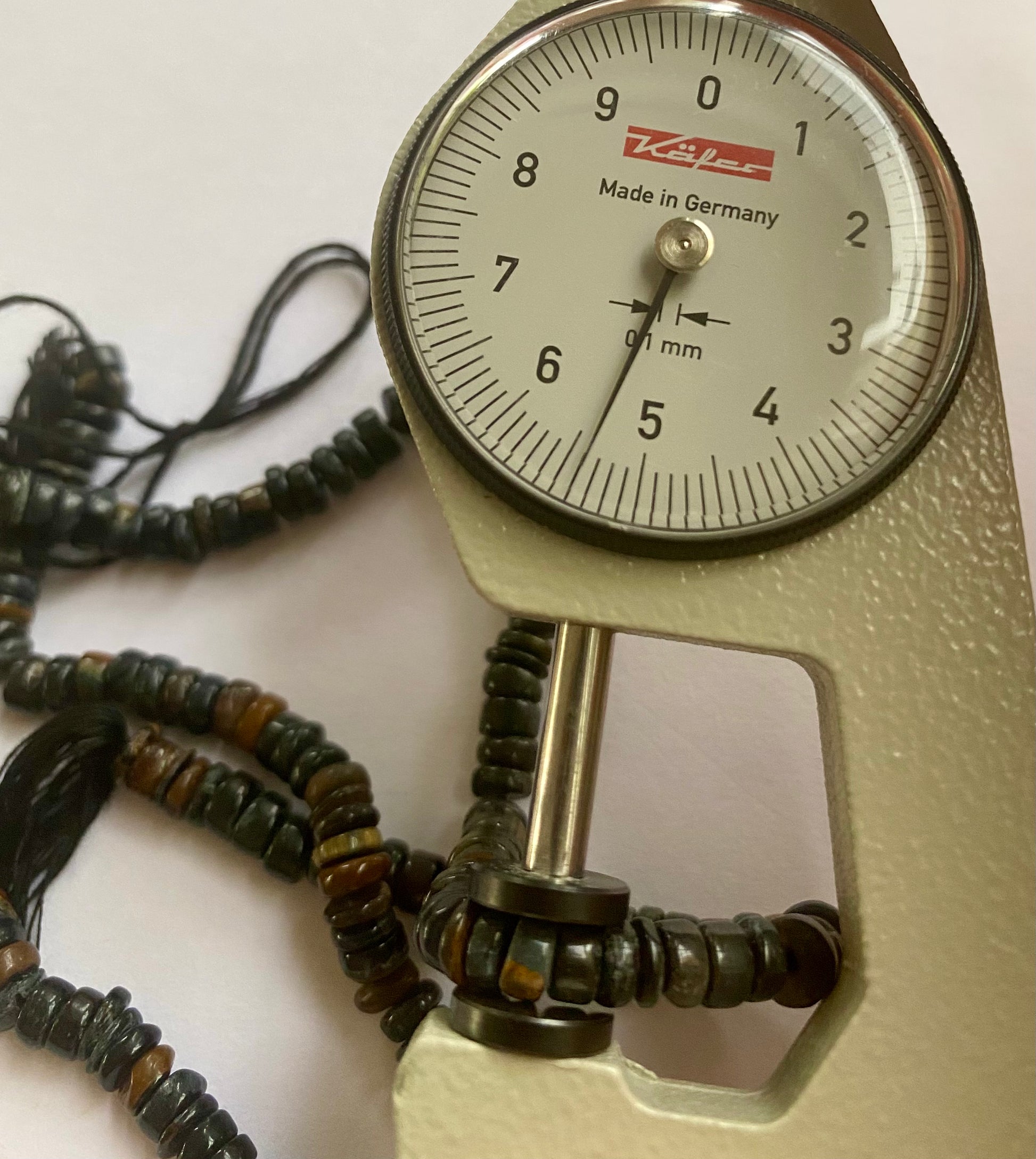 A dial gauge measures the Black Tiger Eye Smooth Wheel 5-5.5mm  gemstone.
