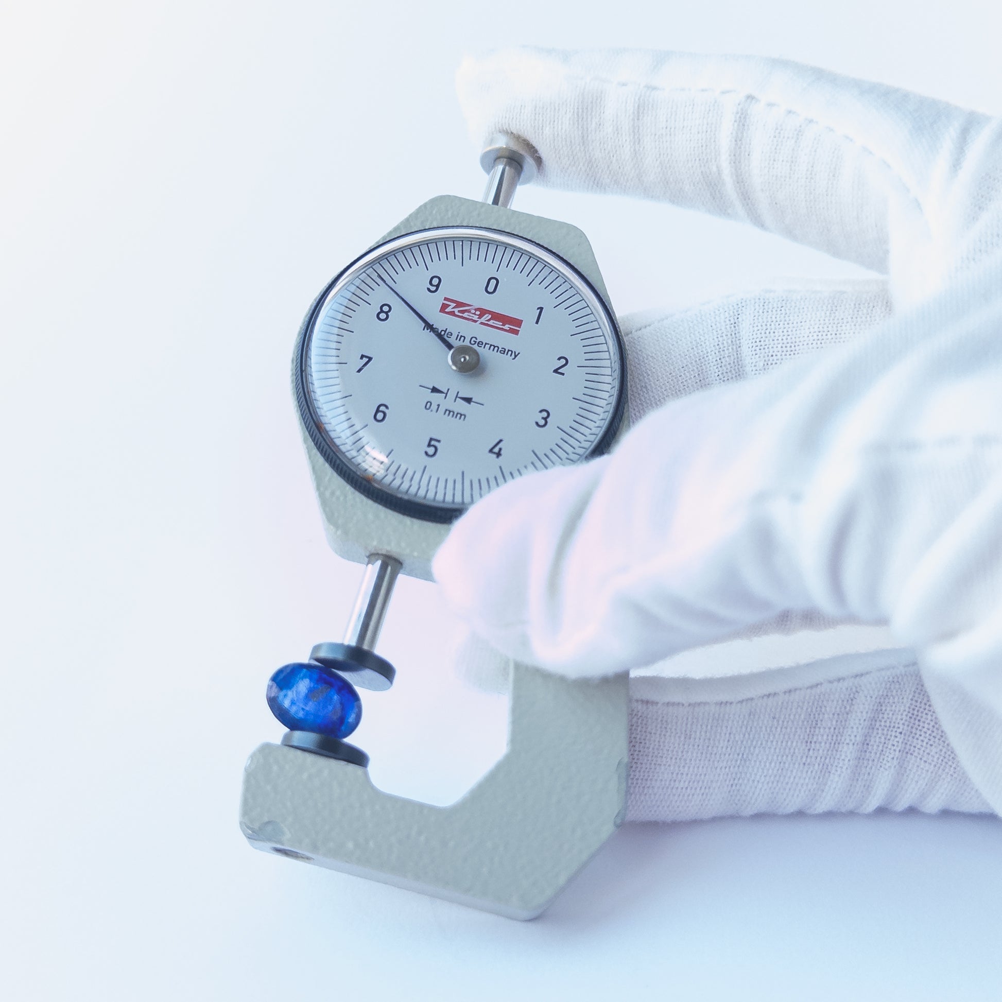 A dial gauge measures the Blue Sapphire faceted oval 11.5mm × 8.4mm gemstone.