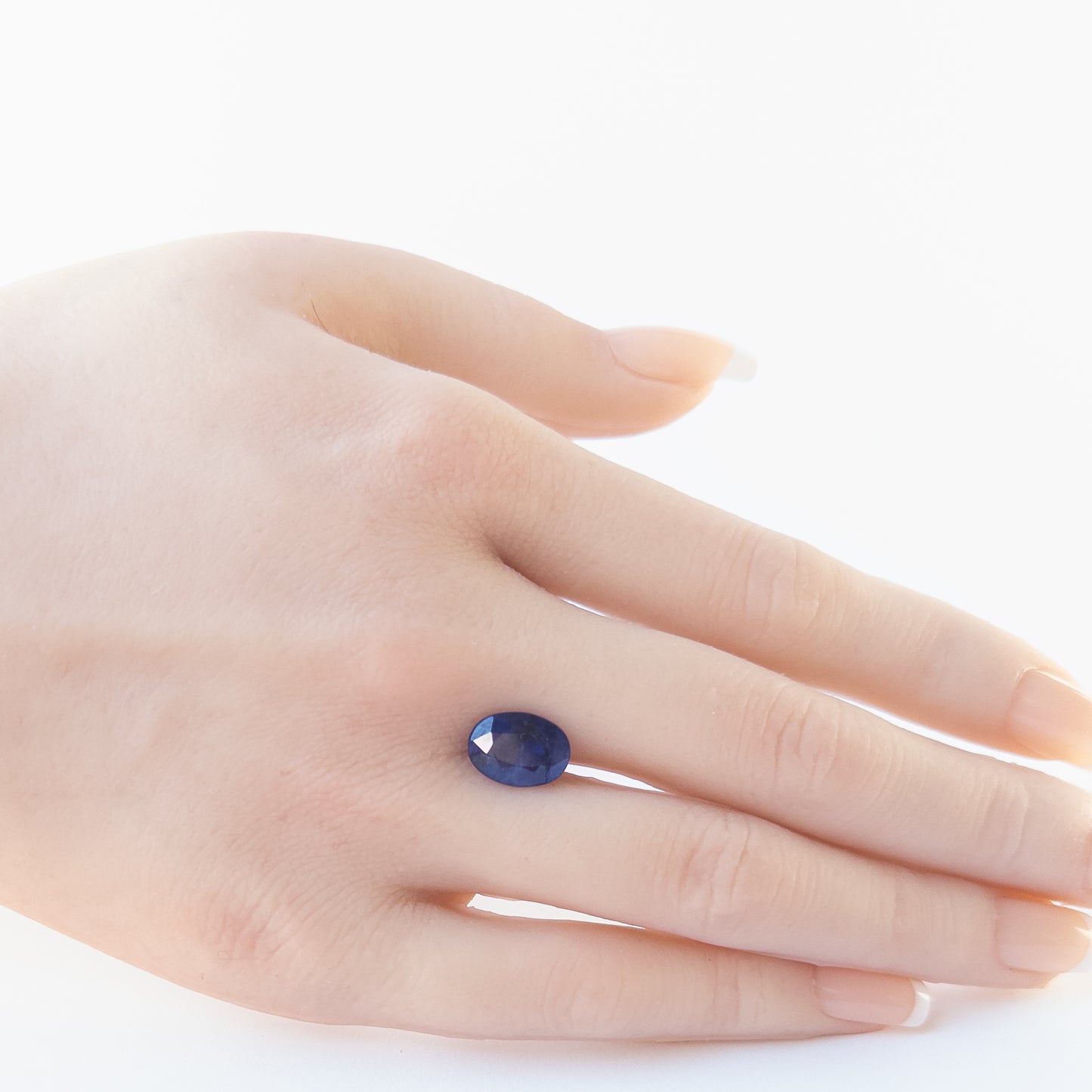 A person holds delicate pieces of Blue Sapphire cabochon, showcasing their faceted oval design.