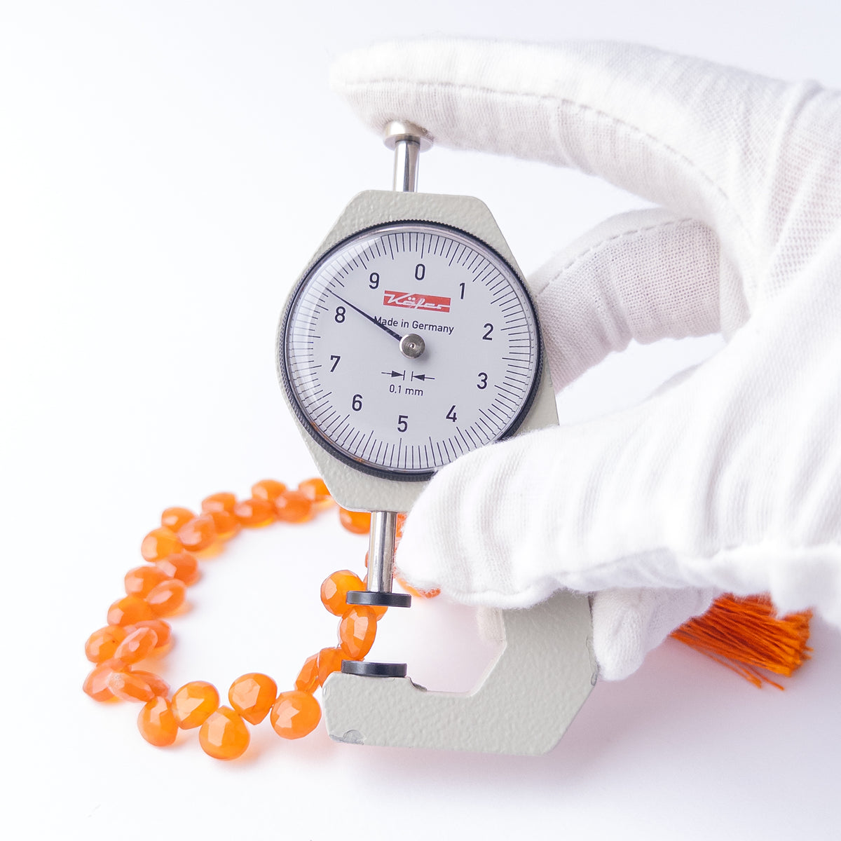 A dial gauge measures the Carnelian Faceted Briolette 7.5-8mm gemstone.