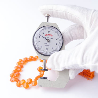 A dial gauge measures the Carnelian Faceted Briolette 7.5-8mm gemstone.