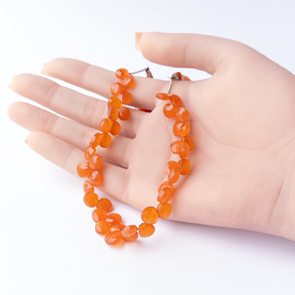 A person holds delicate strands of Carnelian beads, showcasing their faceted briolette design.