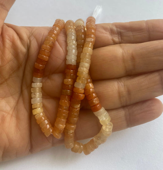 A person holding a strands of smooth Carnelian beads, showcasing their vibrant colour and heishi shape. 