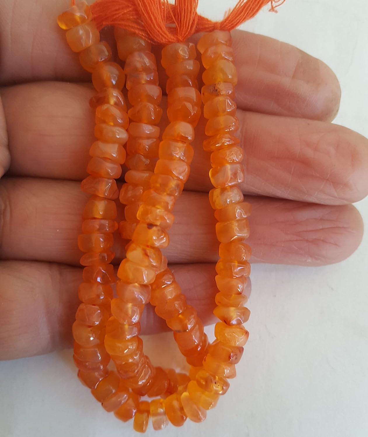 A person holding a strand of smooth wheel carnelian beads, showcasing the colour and shape.