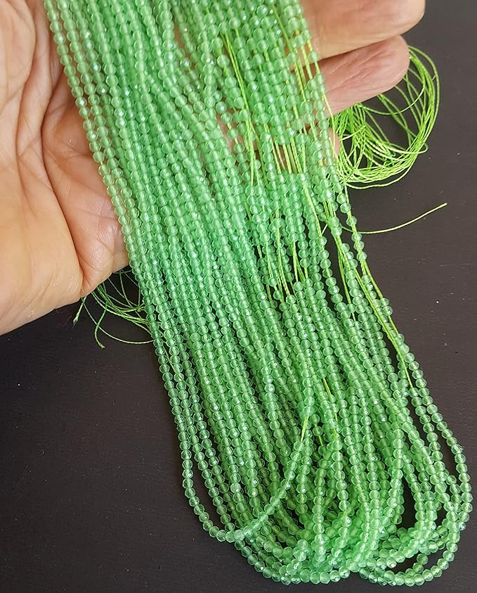  A persons hand showing the close-up of multiple strands of green chalcedony beads, 2.5mm in size, highlighting their faceted rondelle design and rich hue.