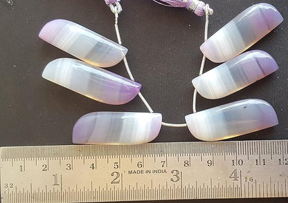 A person measures a purple Chalcedony fancy shaped stone, using a ruler measuring tool.