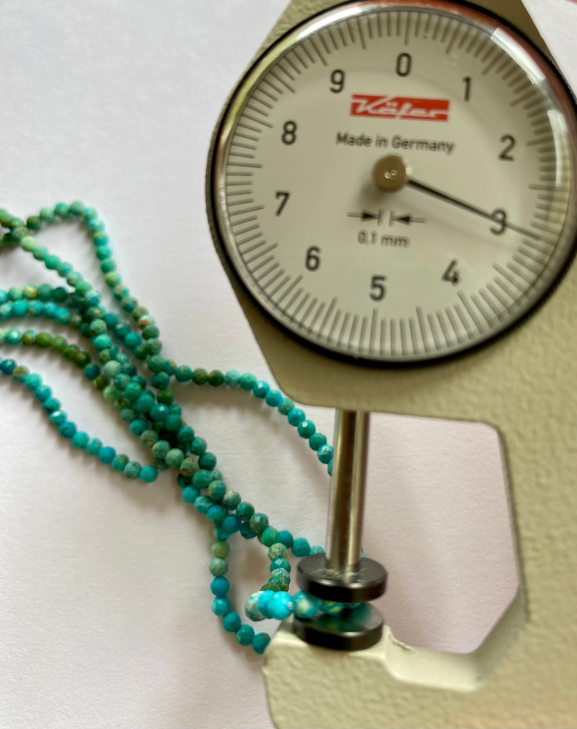 Close-up of a measuring dial gauge alongside faceted rondelle 3mm Chrysocolla  beads in vibrant colour.