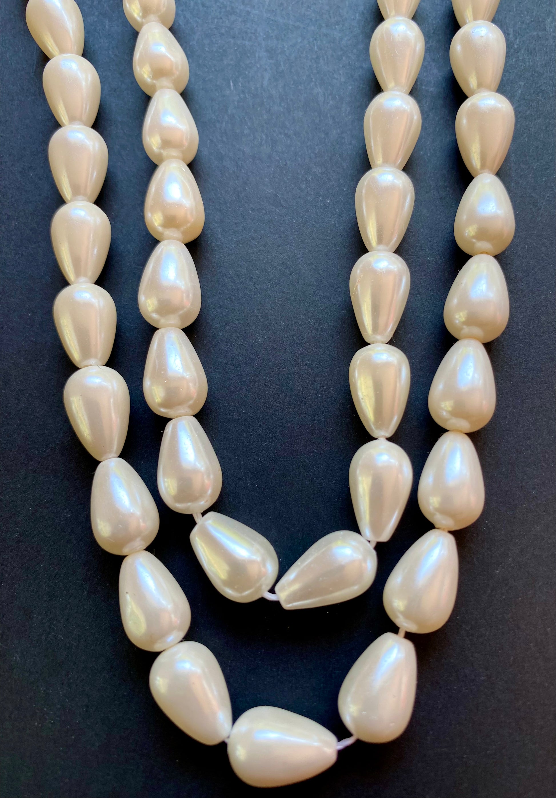 Strand of 8-12mm white freshwater pearls resting on a smooth black surface, showcasing their lustre.
