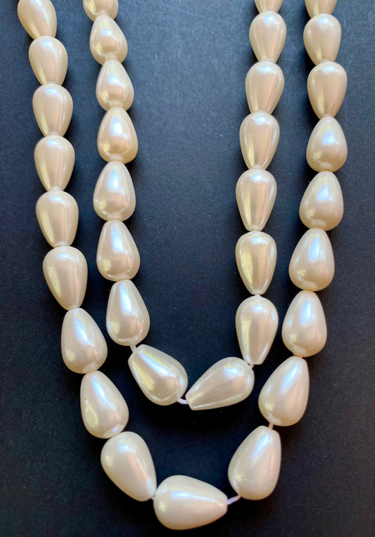 Strand of 8-12mm white freshwater pearls resting on a smooth black surface, showcasing their lustre.