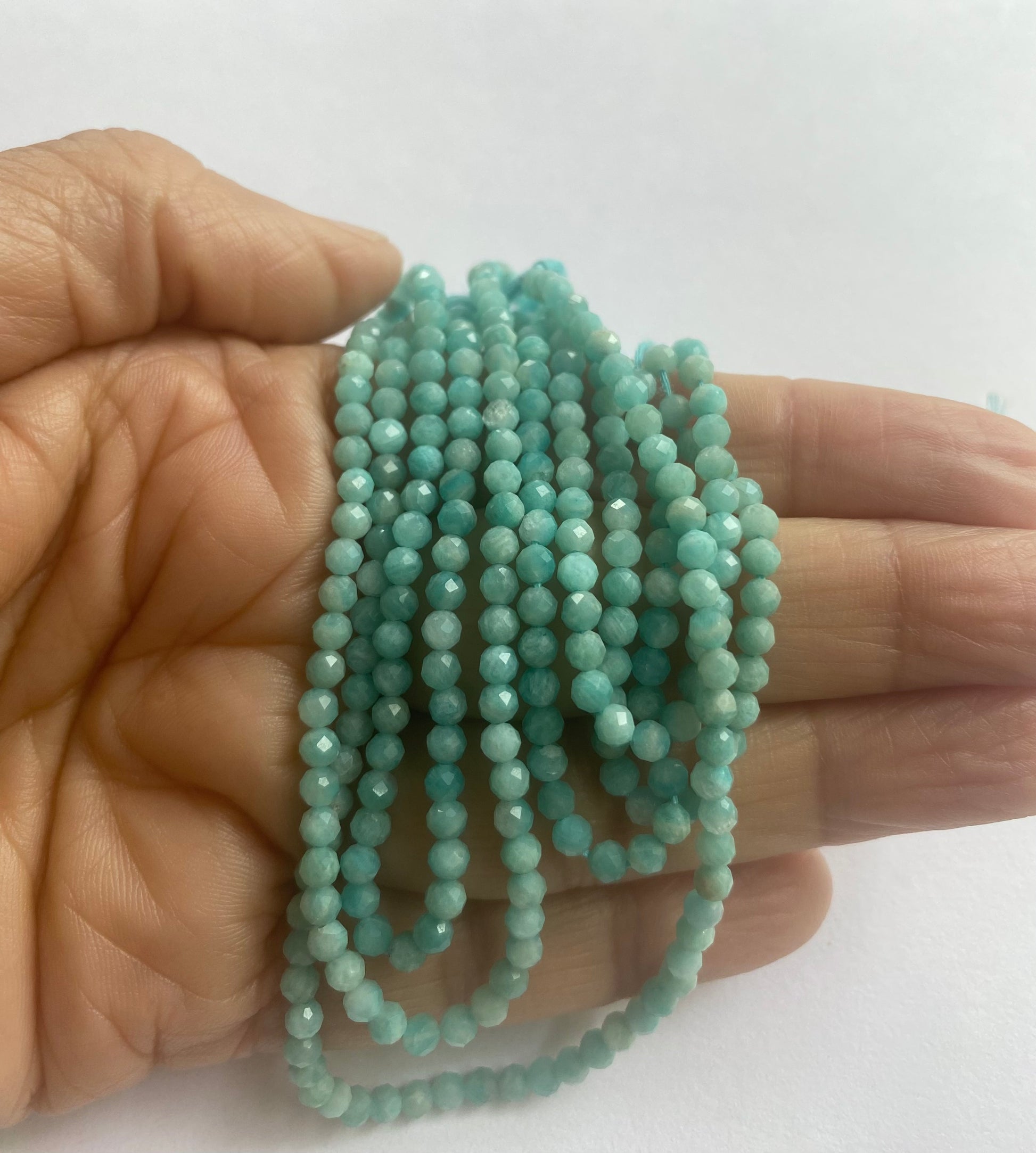  A person holding a strand of Amazonite faceted rondelle beads, measuring 3.4-3.5mm in size.