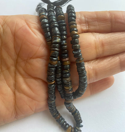  A hand holding a strand of smooth, wheel 5 to 5.5mm black tiger eye beads, showcasing their vibrant colour and elegant design.