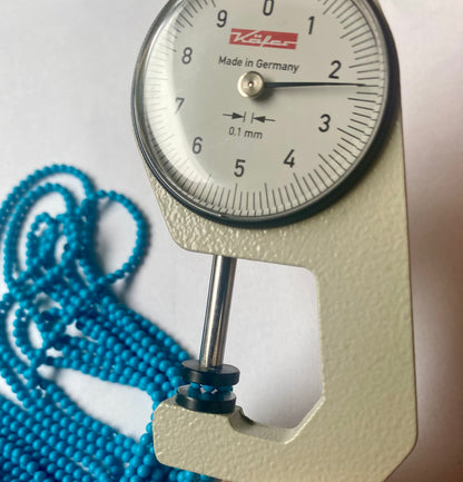 A dial gauge measures the Howlite Turquoise Smooth Round 2.3mm  gemstone.