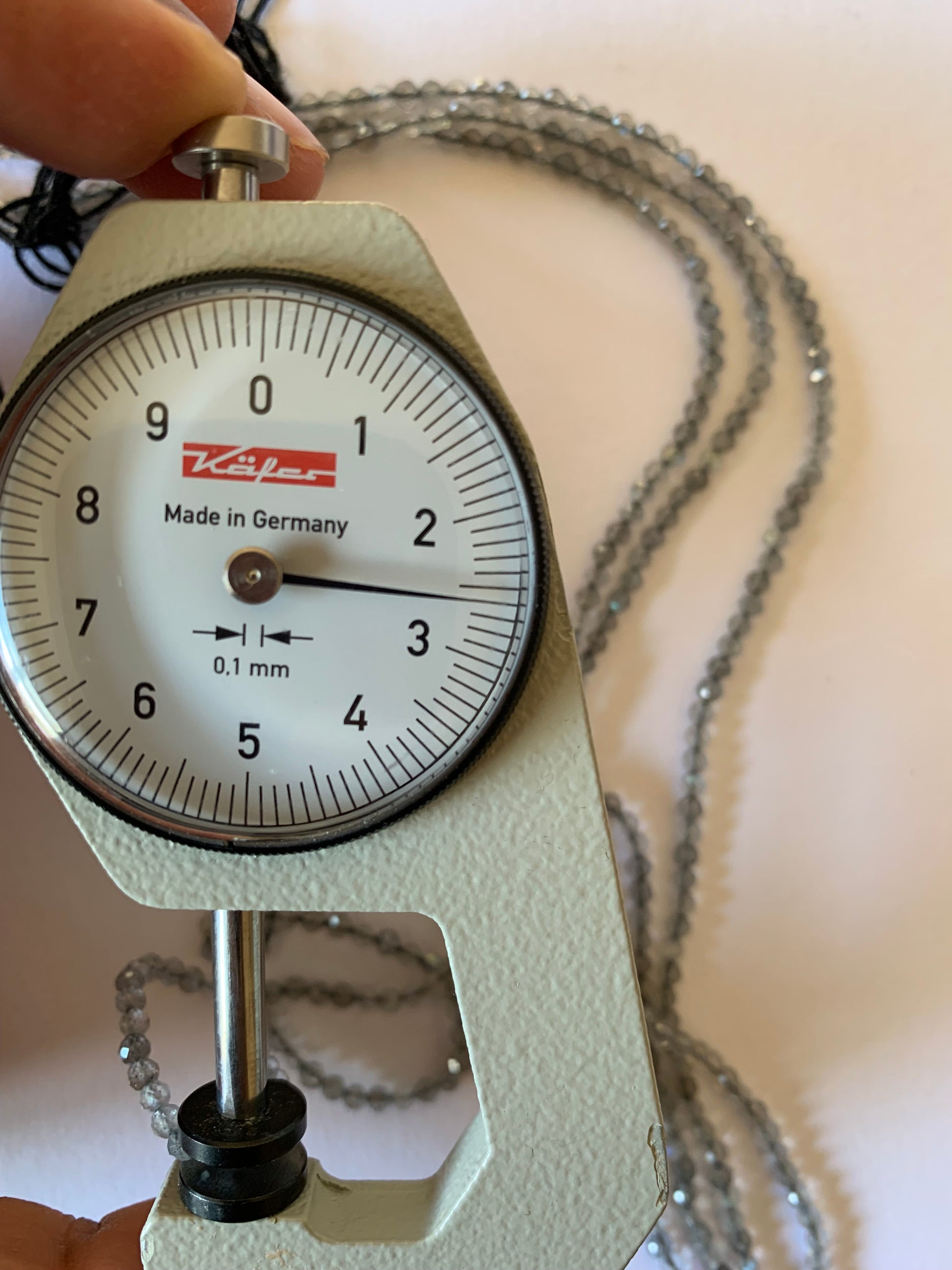 A dial gauge measures the Labradorite Faceted Rondelle 2.5-2.7mm gemstone.