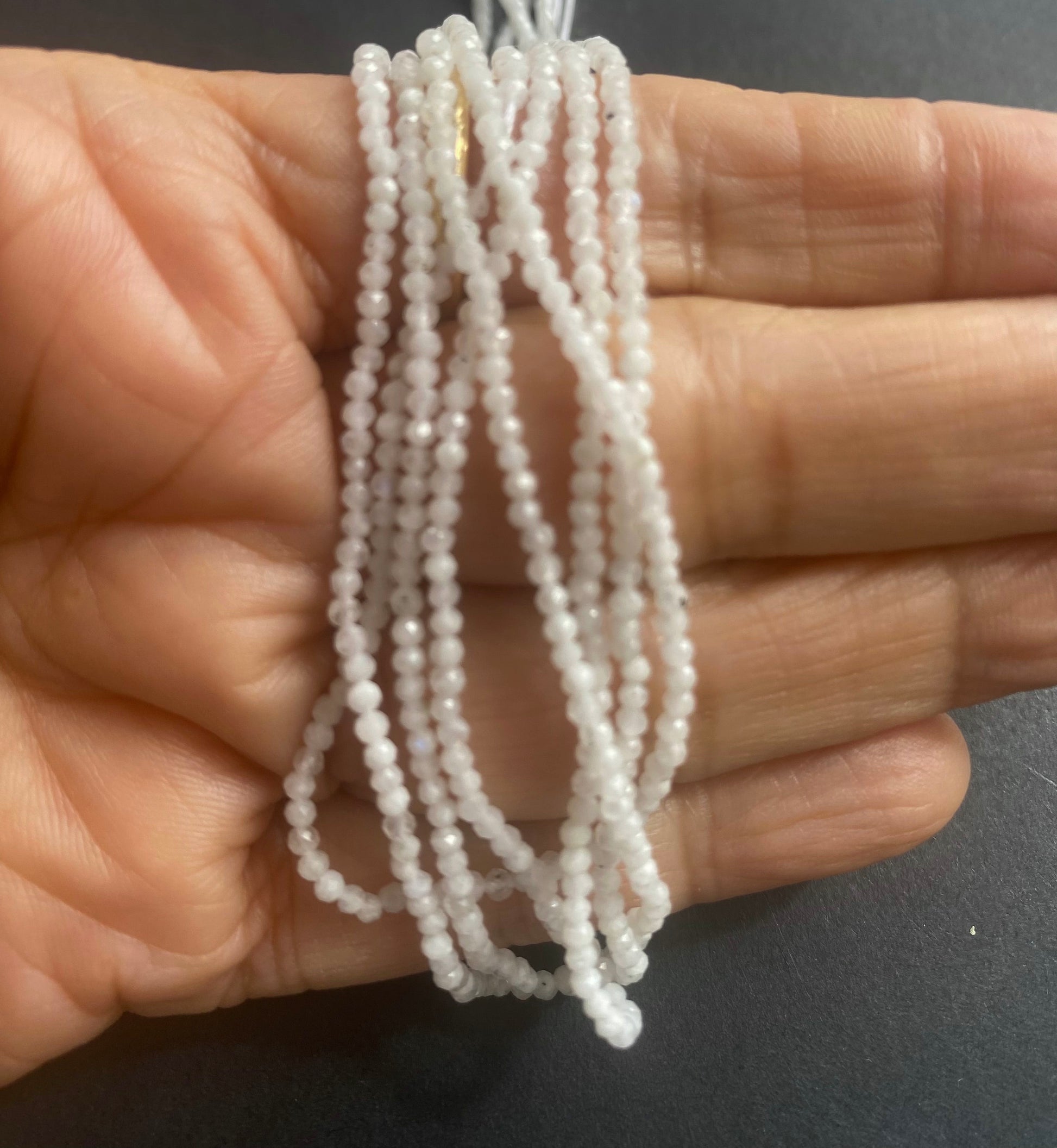 A hand holding a cluster of faceted natural Moonstone stone beads, measuring 2.1mm.