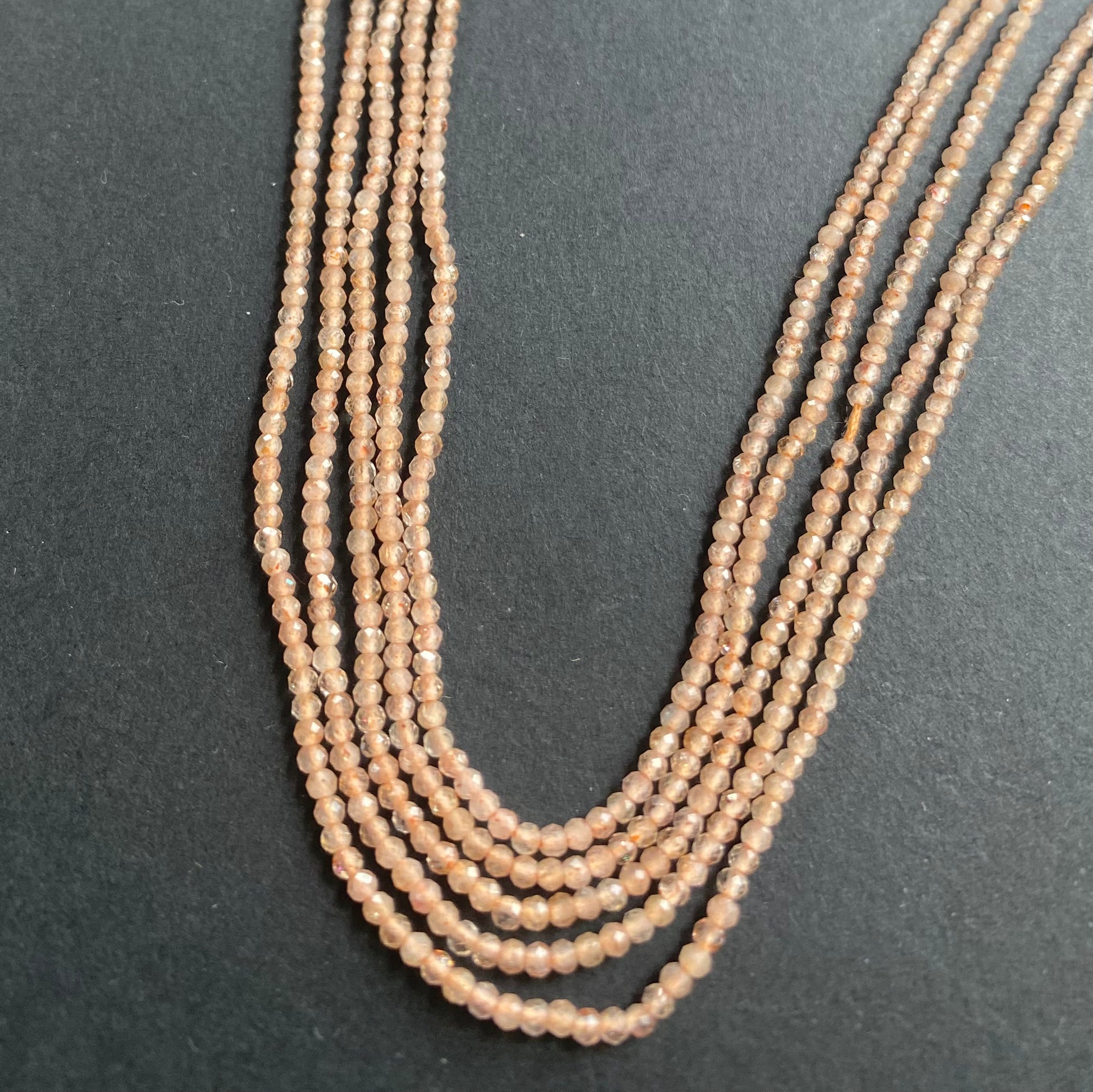 Strands of micro-faceted peach moonstone beads rests elegantly on a smooth black surface, showcasing their delicate shine.