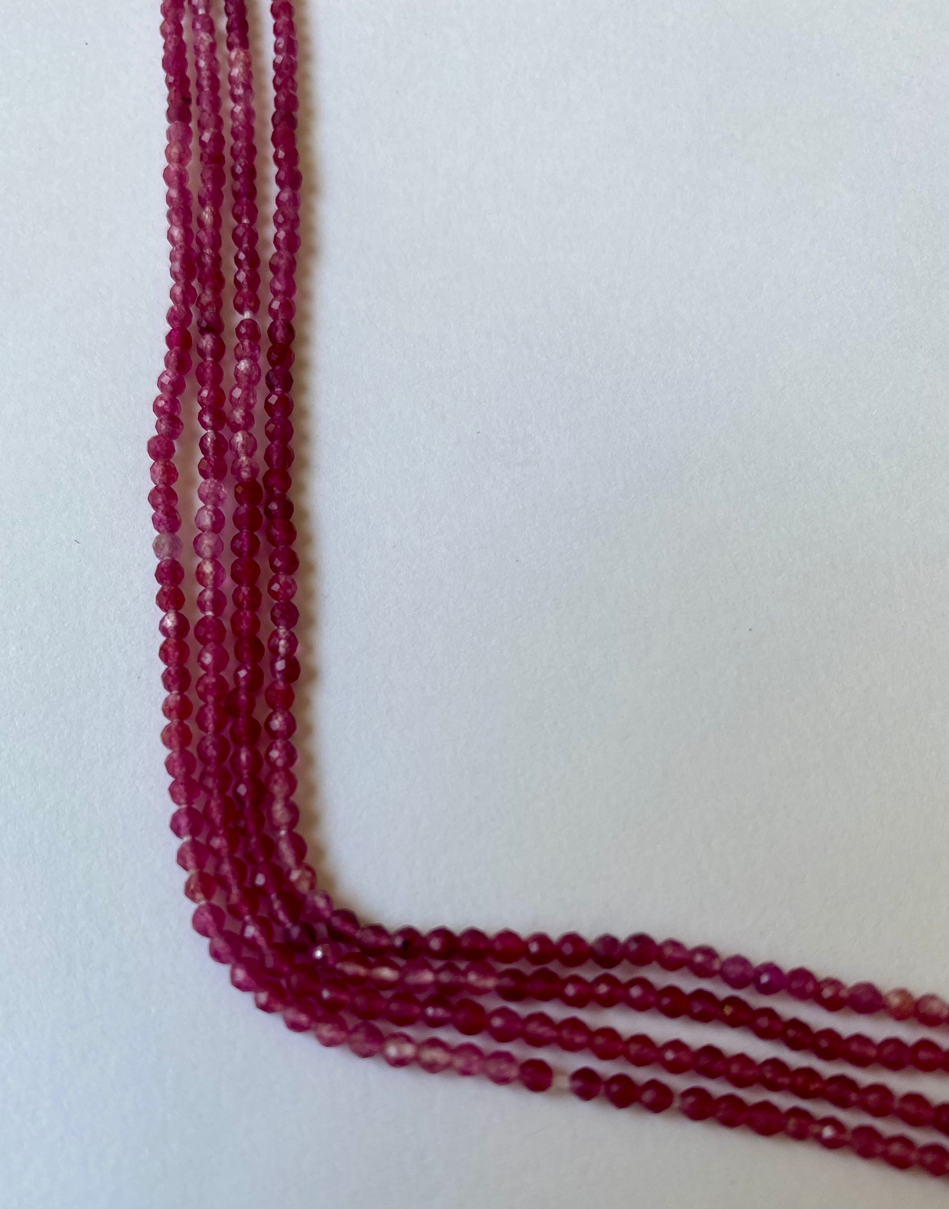 A beautiful strand of 2-2.2mm strawberry quartz beads resting on a clean white surface, showcasing their shine.