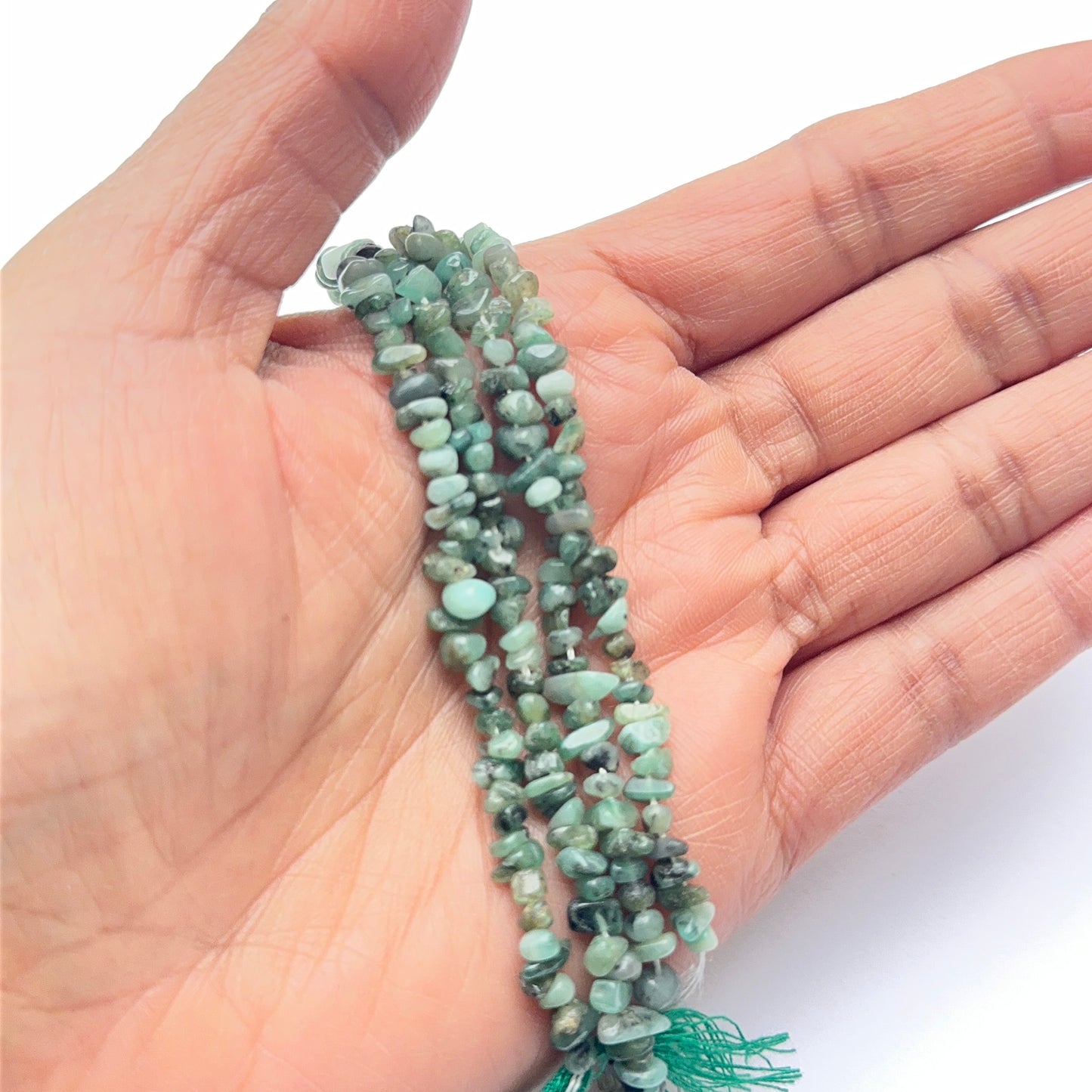 A person holds delicate strands of emerald beads, showcasing their smooth design