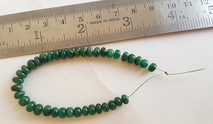 An 5-6mm emerald green natural stone rondelle bead next to a ruler for size reference.