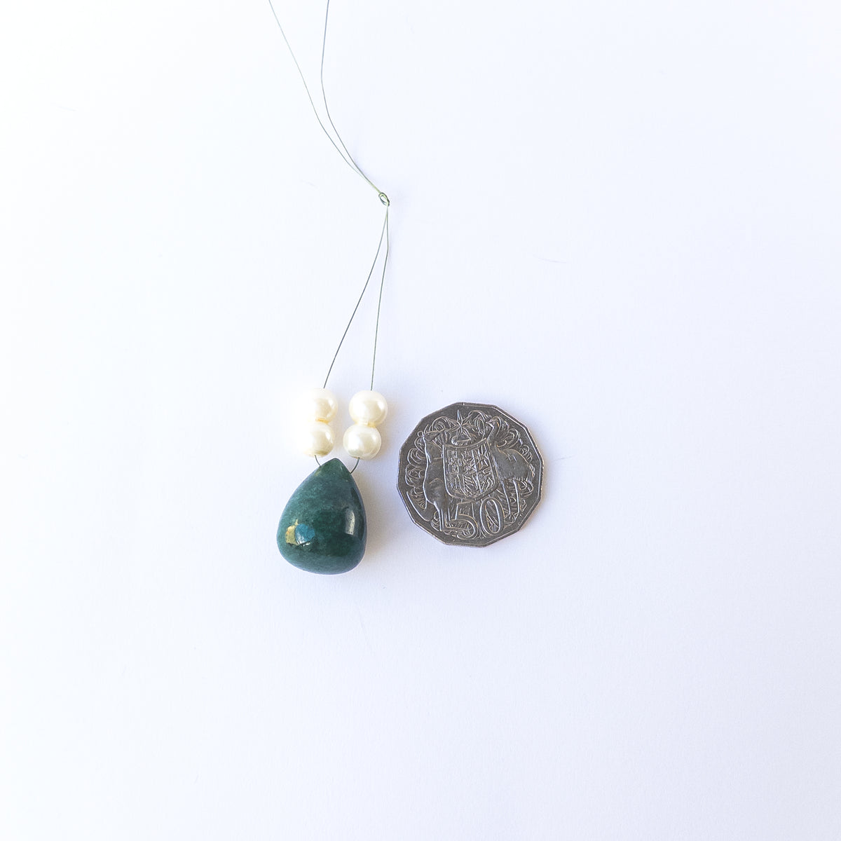 A coin is placed near delicate pieces of Emerald beads for scale.