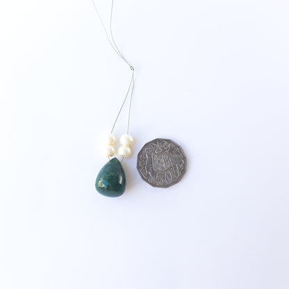 A coin is placed near delicate pieces of Emerald beads for scale.