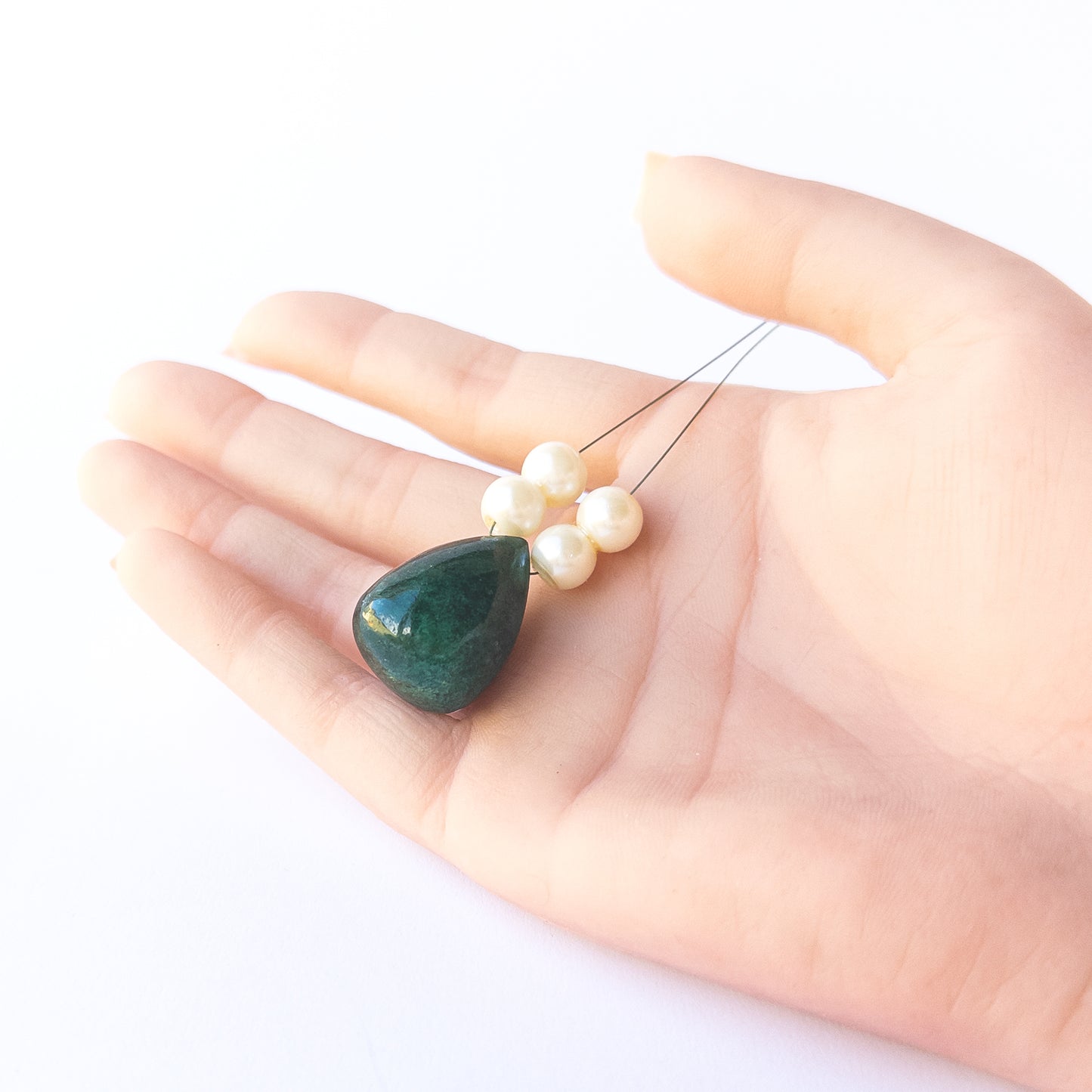 A person holds delicate pieces of Emerald beads, showcasing their smooth teardrop design.