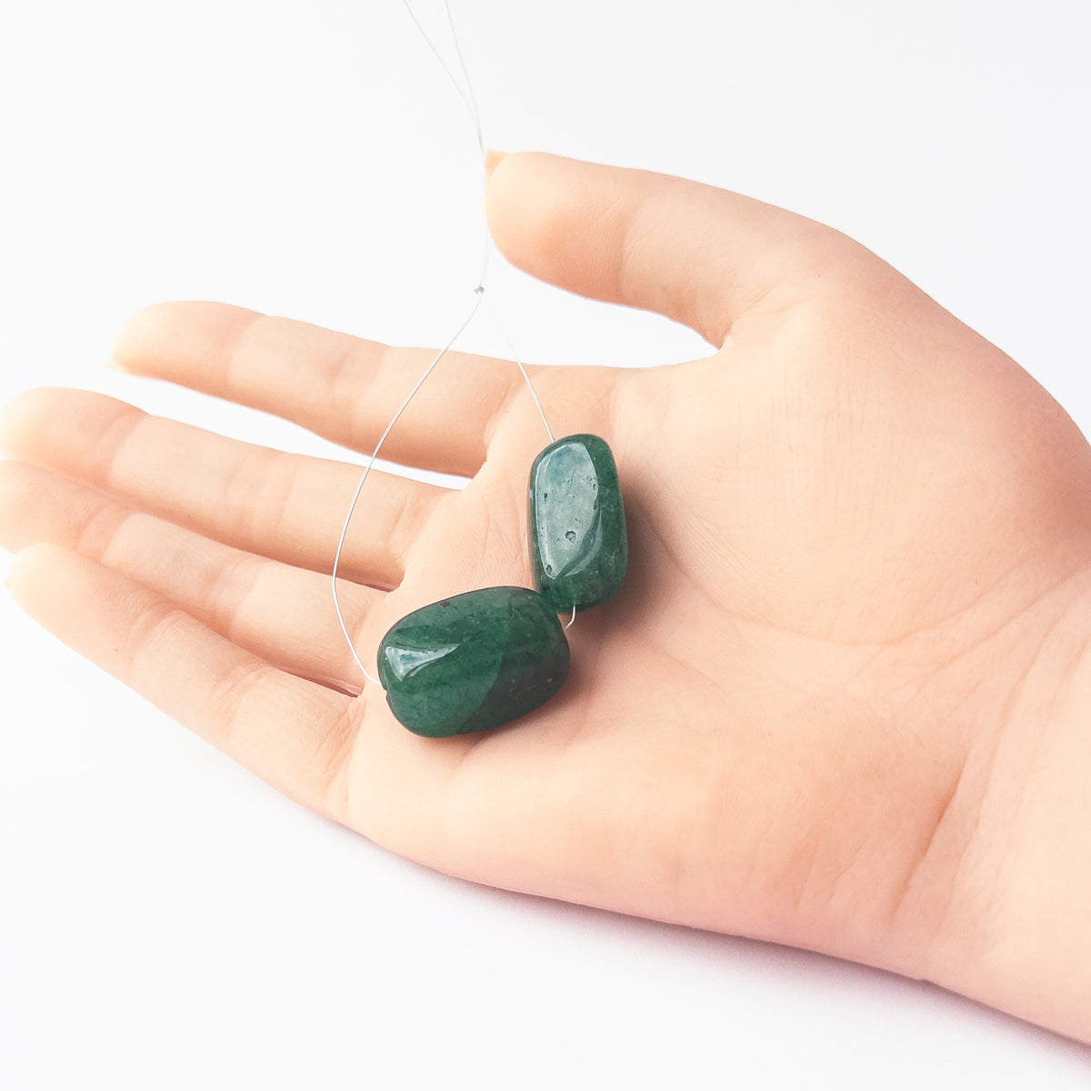 A person holds delicate pieces of Emerald beads, showcasing their smooth tumble design.