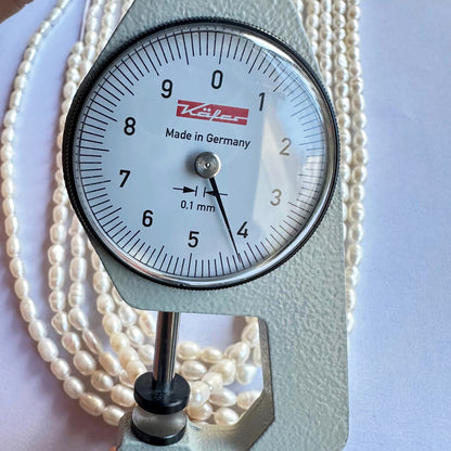 A dial gauge measures the Fresh Water Pearl smooth fancy shape 4mm to 4.5mm gemstone, ensuring size accuracy.
