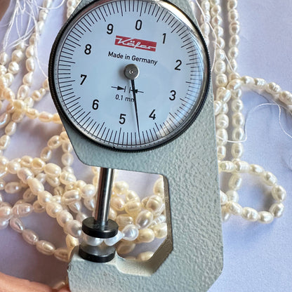 A dial gauge measures the Fresh Water Pearl smooth fancy shape 4mm to 4.5mm gemstone, ensuring size accuracy.