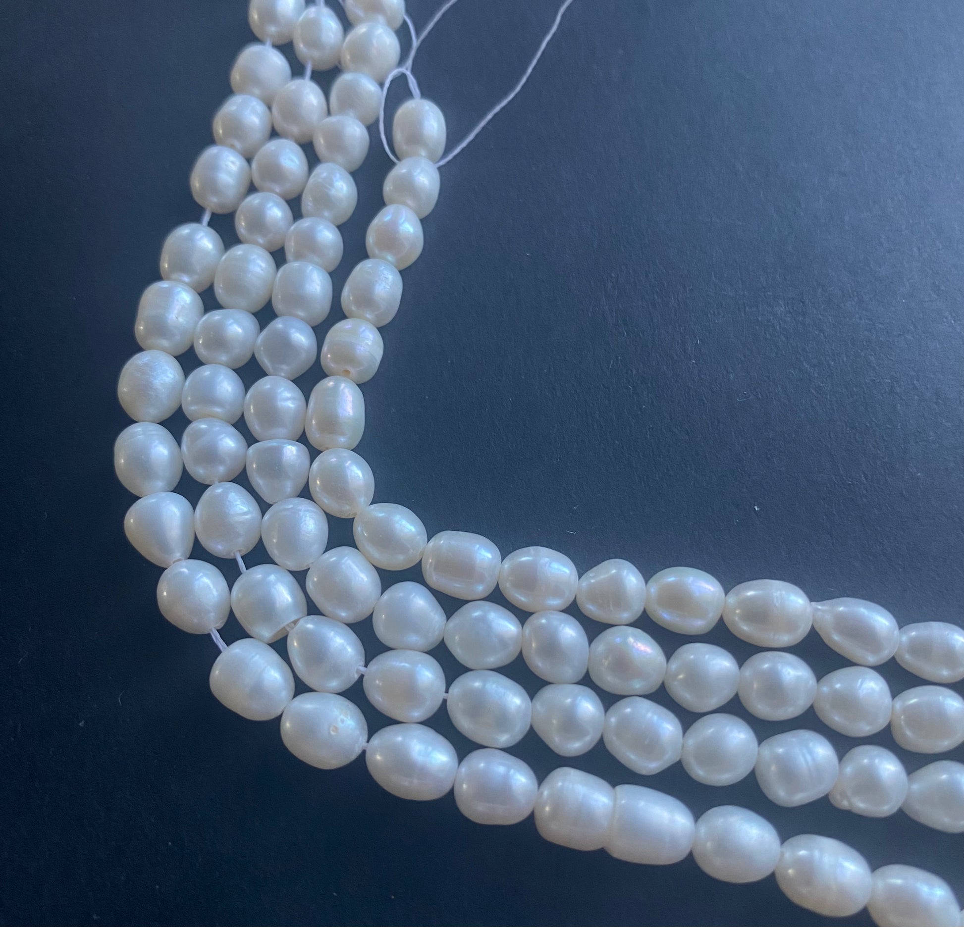 Delicate strands of 6mm freshwater pearl beads elegantly displayed on a smooth black surface.